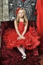 Blonde girl in a red elegant dress with a red hairpin in her hair sitting on an armchair Royalty Free Stock Photo