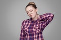 Blonde girl in red, pink checkered shirt, collected bun hairstyle, makeup standing with closed eyes and touching her painful neck Royalty Free Stock Photo