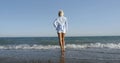 A blonde girl with a short haircut stands on a sandy-pebble beach, wet her feet in the waves of the sea, against the Royalty Free Stock Photo