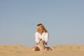 Blonde girl in a shorts and  white shirt is sitting and playing with send in the biggest European dessert. Hot summer. Oleshki san Royalty Free Stock Photo