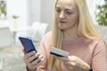 Blonde girl sit on the couch with phone and credit card. concept online shopping Royalty Free Stock Photo