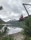 Blonde girl sits sideways in checkered red plaid.Beautiful lake,forest,mountains Royalty Free Stock Photo