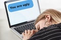 Blonde girl sleeping near laptop with you are ugly message on screen, cyberbullying concept.