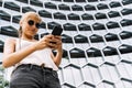 Blonde girl standing in front of a modern building texting with the mobile