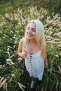 Blonde girl is standing in the grass in a white dress smiling, top view