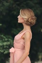 Blonde girl with stylish hairstyle in pink dress. portrait of young woman in spring park. side view Royalty Free Stock Photo