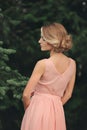 Blonde girl with stylish hairstyle in pink dress. portrait of young woman in spring park. side view Royalty Free Stock Photo