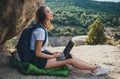 Blonde girl after walk in mountains rests listening to music in headphones typing on a laptop in nature, traveler woman plans Royalty Free Stock Photo