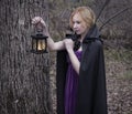 Blonde girl wearing mantle and holding lantern in the forest
