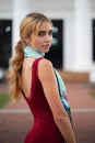 Blonde girl wearing a maroon dress and blue scarf standing in an urban setting Royalty Free Stock Photo