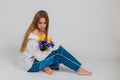 a blonde girl in a white shirt and blue jeans holds a bouquet of tulips and irises sitting on a white background. March 8. bouquet Royalty Free Stock Photo