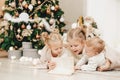 3 blonde girls lie on the floor by the Christmas tree and read a book. cozy evenings with a book by the tree. Girlfriends read a