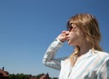 Blonde in glasses and a light shirt against a blue sky