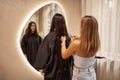 Blonde hairdresser cuts her female client hair in a salon. brunette young woman looks into a huge mirror when her
