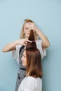 Blonde hairdresser lady trimming client`s hair ends over blue