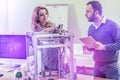 Blonde-haired beautiful officer worker fixing 3D printer standing near colleague