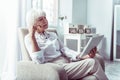 Blonde-haired elderly lady feeling thoughtful reading local news on tablet