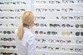 Blonde-haired ophthalmologist putting glasses on shelves in optical store