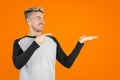 Blonde handsome man pointing with finger at his palm for copy space at right. Orange isolated background