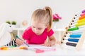 Blonde happy little girl drawing siitting by the white table in light room with wooden colorful abacus. Preschool education, early