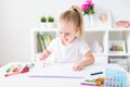 Blonde happy little girl with ponytale drawing and writing lsitting by the white table in light roon. Preschool education, early Royalty Free Stock Photo