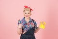 Blonde happy smiled female in pin-up style holding yellow latex gloves and wrench isolated on pastel-pink background.