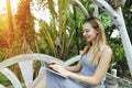 Blonde happy woman uses laptop for work on sunny day, background of sunshine green palms in Thailand, Phuket travel