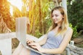 Blonde happy woman uses pc computer for work on sunny day, background of sunshine green palms in Thailand, Phuket travel