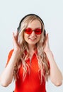 Blonde in headphones with closed eyes. Girl in a red T-shirt and glasses on a white background. Royalty Free Stock Photo