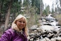 Blonde hiker poses by Whitney Portal Falls, a waterfall near the trailhead for Mt. Whitney in California