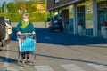 Blonde italian woman with shopping cart and bags goes to a grocery store. Lady wears a face mask to protect herself from covid19