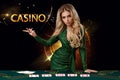 Lady in green dress is showing inscription casino, leaning on playing table with cards on it, posing on black background