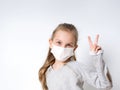 Blonde little girl in gray jumper and medical mask, posing isolated on white. She showing victory hand. Coronavirus