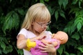 A blonde little girl puts her belly button to bed. A child plays with a doll. Royalty Free Stock Photo