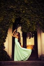 Blonde with a long curly hair in a long evening dress in motion outdoors near retro vintage building all in leaves in summer Royalty Free Stock Photo