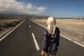 Blonde long hair girl viewed fromback walk on a long straight asphalt road - concept of freedom and independence - hope and future Royalty Free Stock Photo