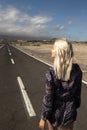 Blonde long hair girl viewed fromback walk on a long straight asphalt road - concept of freedom and independence - hope and future Royalty Free Stock Photo