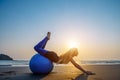 Blonde with long hair makes Pilates on the beach during sunset against the sea. Young flexible happy woman doing fitness exercises Royalty Free Stock Photo