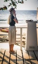 Blonde in long skirt standing on the wooden bridge on the background of the morning sea and adjusts her earrings. A