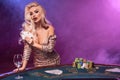 Blonde woman with a perfect hairstyle and bright make-up is posing with playing cards in her hands. Casino, poker.