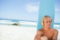 Blonde man sitting in front of his surfboard while looking towards the side Royalty Free Stock Photo