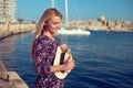 Blonde mediterranean traveler woman holding hat at pier