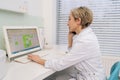 Blonde middle-aged woman general practitioner sit at desk in clinic office looking at laptop screen, discuss medical Royalty Free Stock Photo