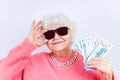 blonde old lady wear pinl sweater and sunglasses showing money isolated white background