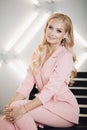 Blonde in pink smart suit sitting on stairs and posing Royalty Free Stock Photo