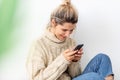 Blonde positive young woman smiling during playing the games on cellphone. Happy female chatting with her boyfriend, looking at Royalty Free Stock Photo