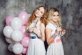 Blonde and redhead. Two young charming girlfriends at the party with balloons. On gray textured background Royalty Free Stock Photo