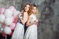 Blonde and redhead. Two young charming girlfriends at the party with balloons. On gray textured background Royalty Free Stock Photo