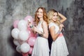 Blonde and redhead. Two young charming girlfriends at the party with balloons. On gray textured background Royalty Free Stock Photo