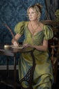 A Regency woman wearing a green shot silk dress and sitting at a table writing a letter with a quill Royalty Free Stock Photo